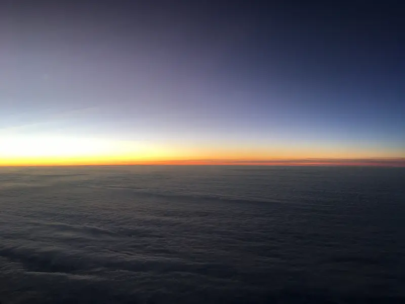 A photo of the sunrise, taken through the window of an airplane, above the clouds, somewhere over the USA