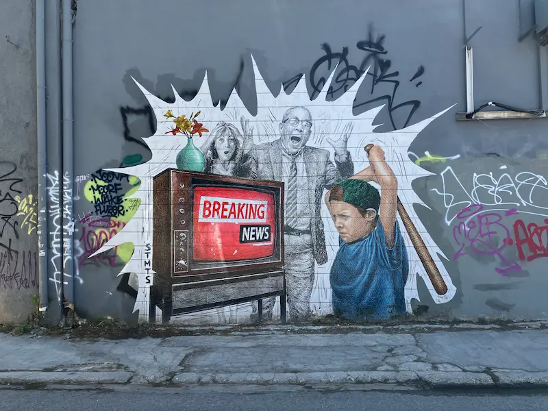 Graffiti of a boy smashing a television that says “Breaking News” on a wall in Athens, Greece