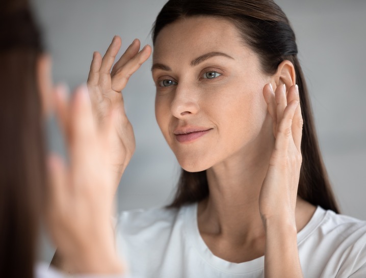 Lady with clear and smooth skin looking in the mirror